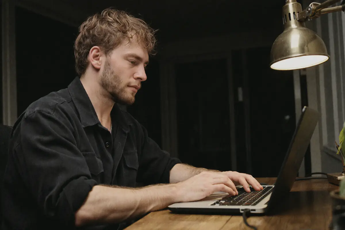 Jules tippt im Schein einer Schreibtischlampe auf einem Laptop.